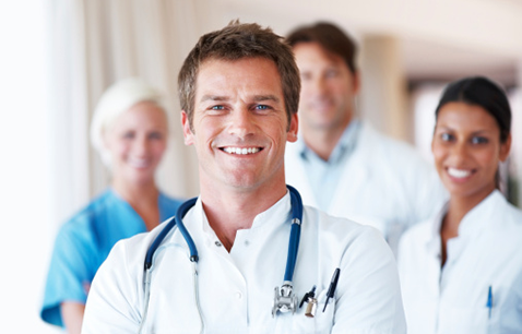 Image focused on white male doctor wearing white shirt and blue stethoscope with 3 out of focus colleagues behind him 2 female and 1 male.