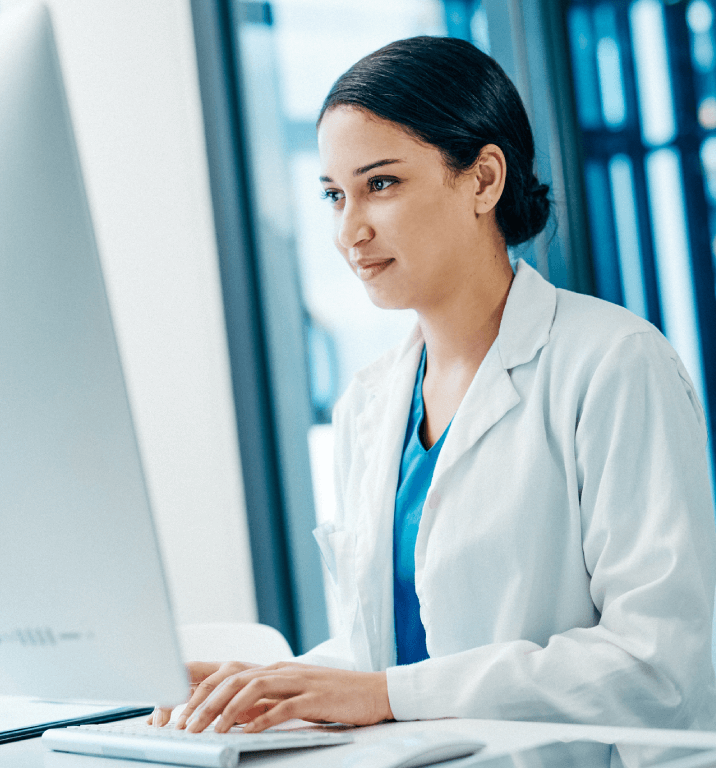 Female doctor with dark hair working on a desktop computer, symbolizing cme online learning convenience.